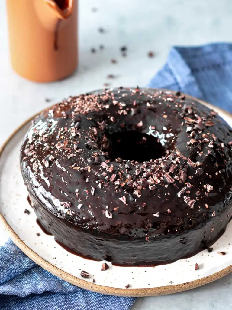 bolo de chocolate vegano servido em prato com cobertura de calda de chocolate e nibs de cacau