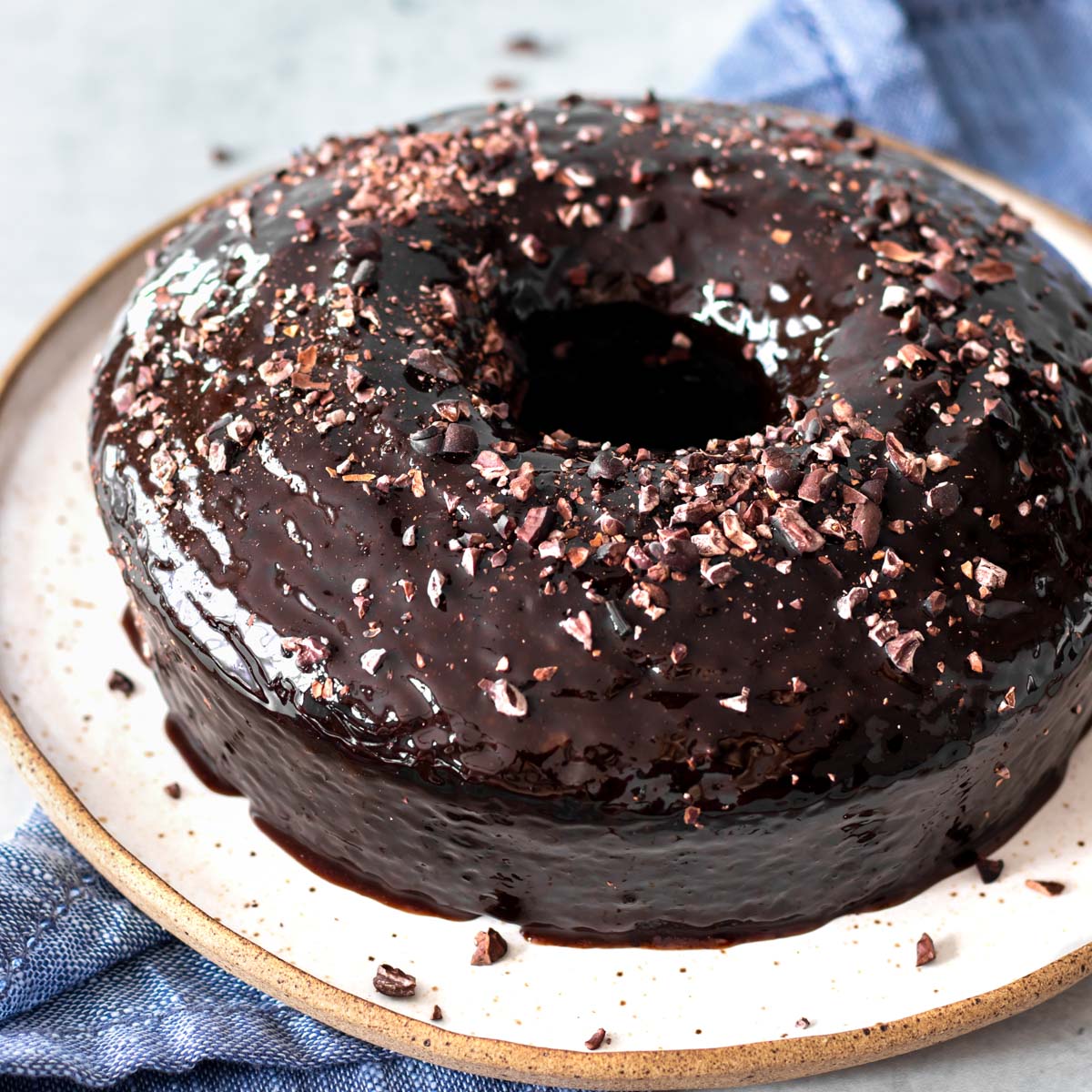 bolo de chocolate vegano servido em prato com cobertura de calda de chocolate e nibs de cacau