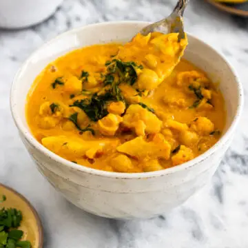 colher retirando curry de grão-de-bico de tigela, mostrando sua textura cremosa