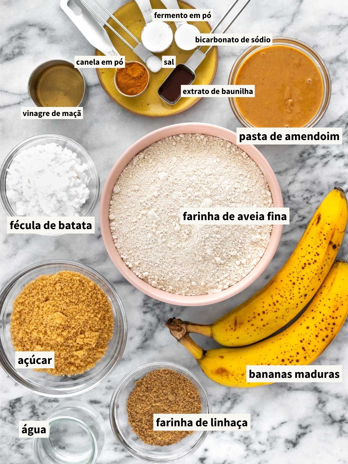 ingredientes para fazer bolo de banana sem glúten, incluindo farinha de aveia fina, banana, pasta de amendoim, açúcar, farinha de linhaça, água filtrada, canela em pó, sal, extrato de baunilha, vinagre de maçã, fécula de batata, fermento químico em pó e bicarbonato de sódio