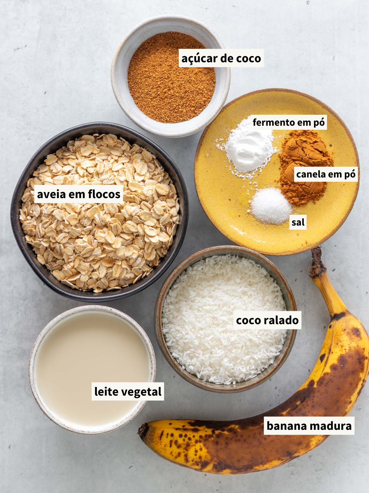 ingredientes para fazer bolo de mingau de aveia assado, incluindo banana madura, açúcar de coco, canela em pó, sal, fermento químico, leite vegetal, aveia em flocos grossos e coco ralado
