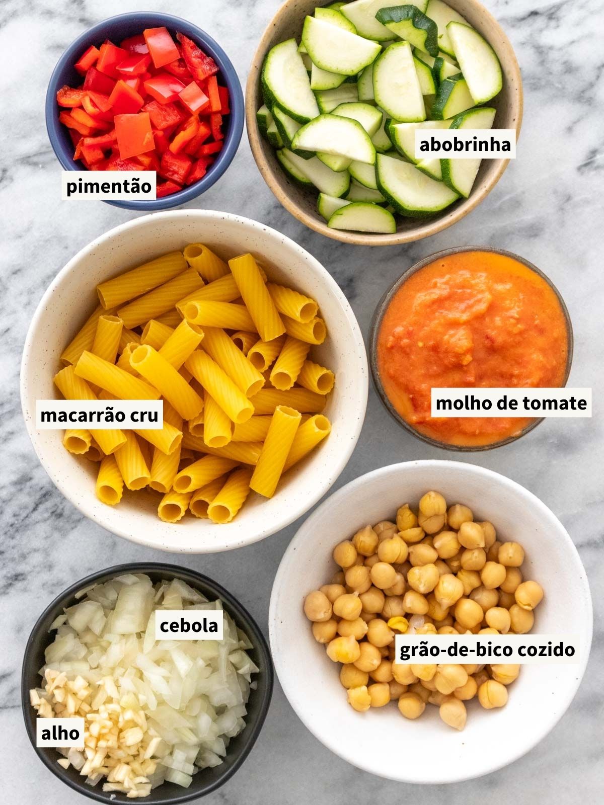 ingredientes para fazer macarrão com vegetais e molho vermelho, incluindo cebola, alho, pimentão vermelho, sal, massa curta, grão-de-bico cozido, abobrinha e molho de tomate assado