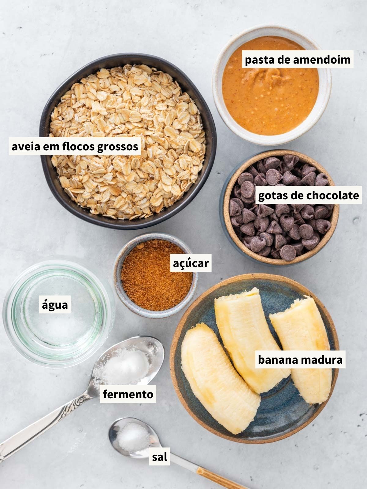ingredientes para fazer muffin de banana com aveia, incluindo aveia em flocos grossos, banana madura, açúcar de coco, pasta de amendoim natural, fermento químico em pó, sal, água filtrada e gotas de chocolate