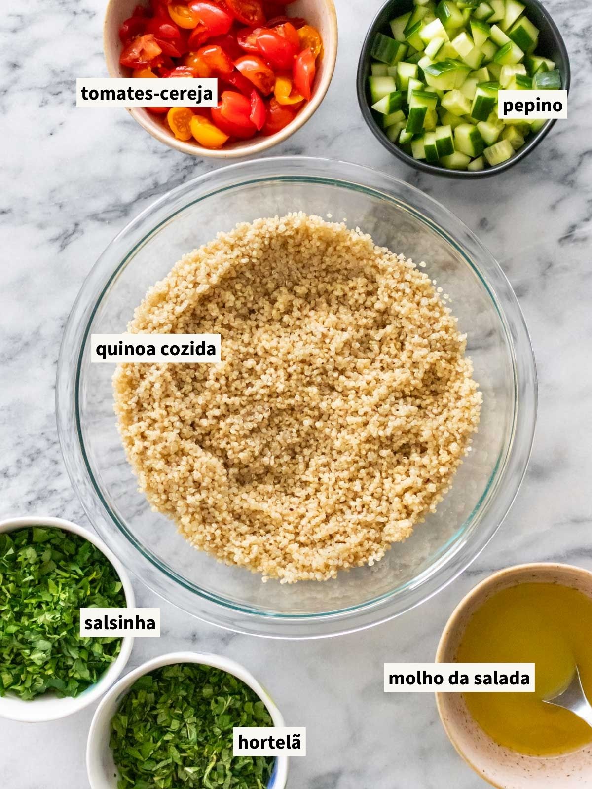 ingredientes para fazer tabule de quinoa, incluindo quinoa cozida, tomate cereja, pepino, salsinha, hortelã e molho de azeite de oliva, suco de limão siciliano, alho, sal e pimenta-do-reino moída