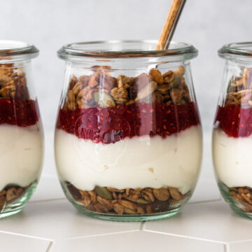 iogurte com granola servido em copinho com camada de granola, iogurte, geleia de morango e mais granola por cima