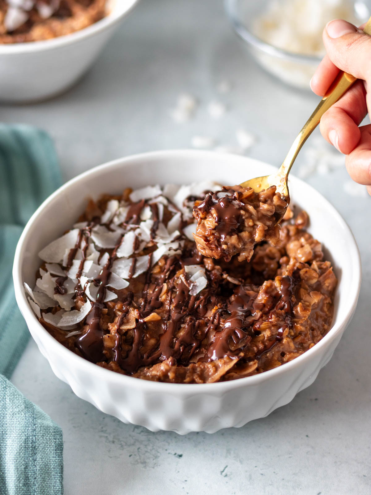 mingau de aveia com chocolate e coco servido com coco em fitas e chocolate derretido, com uma colher tirando uma porção e mostrando sua textura cremosa