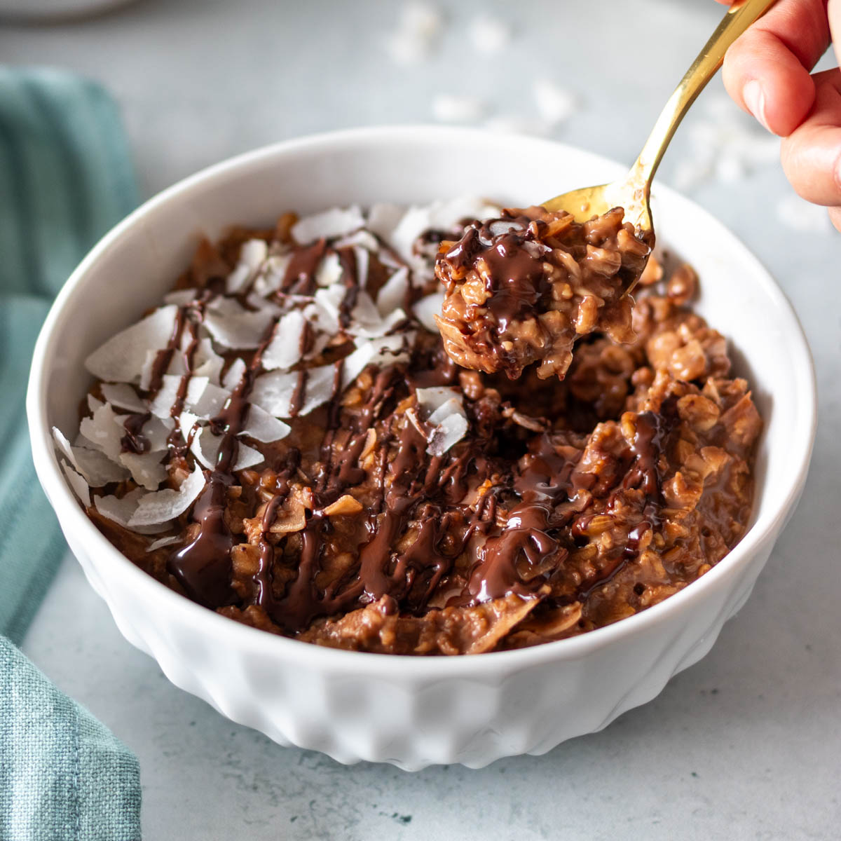 mingau de aveia com chocolate e coco servido com coco em fitas e chocolate derretido, com uma colher tirando uma porção e mostrando sua textura cremosa