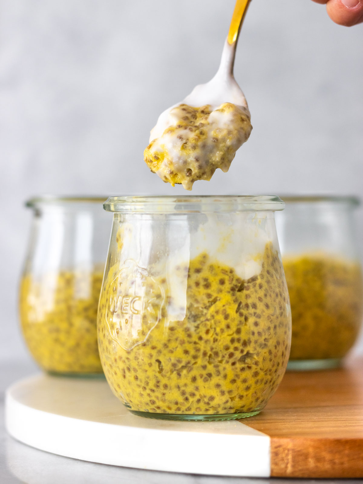 colher retirando porção de pudim de chia de manga servido com iogurte de coco