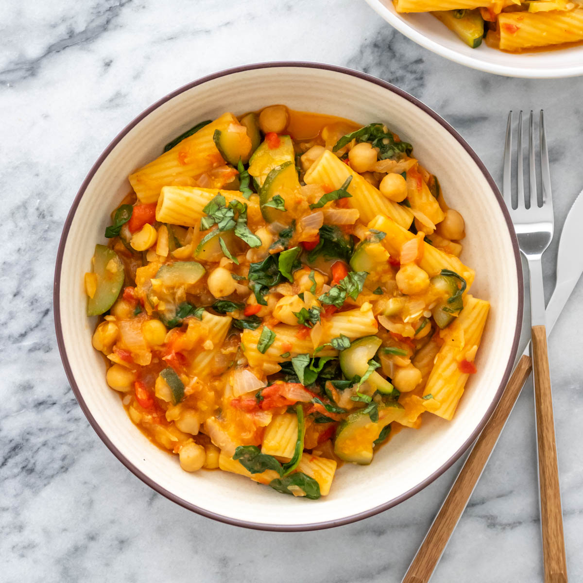 macarrão com vegetais e molho vermelho servido em um prato com manjericão fresco picado