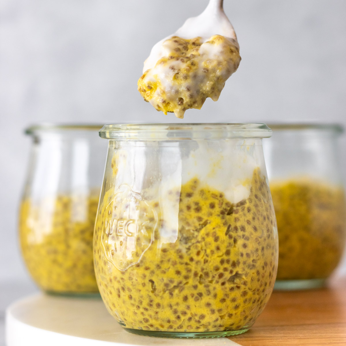 colher retirando porção de pudim de chia de manga servido com iogurte de coco
