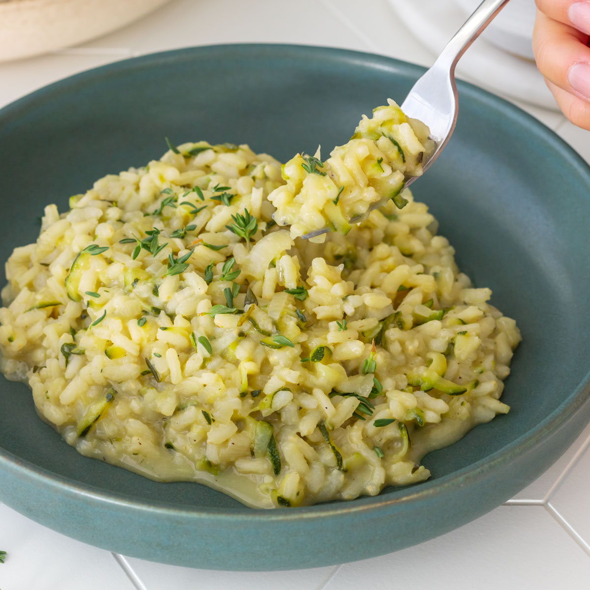 garfo retirando uma porção de risoto de abobrinha com tomilho de um prato, mostrando sua cremosidade
