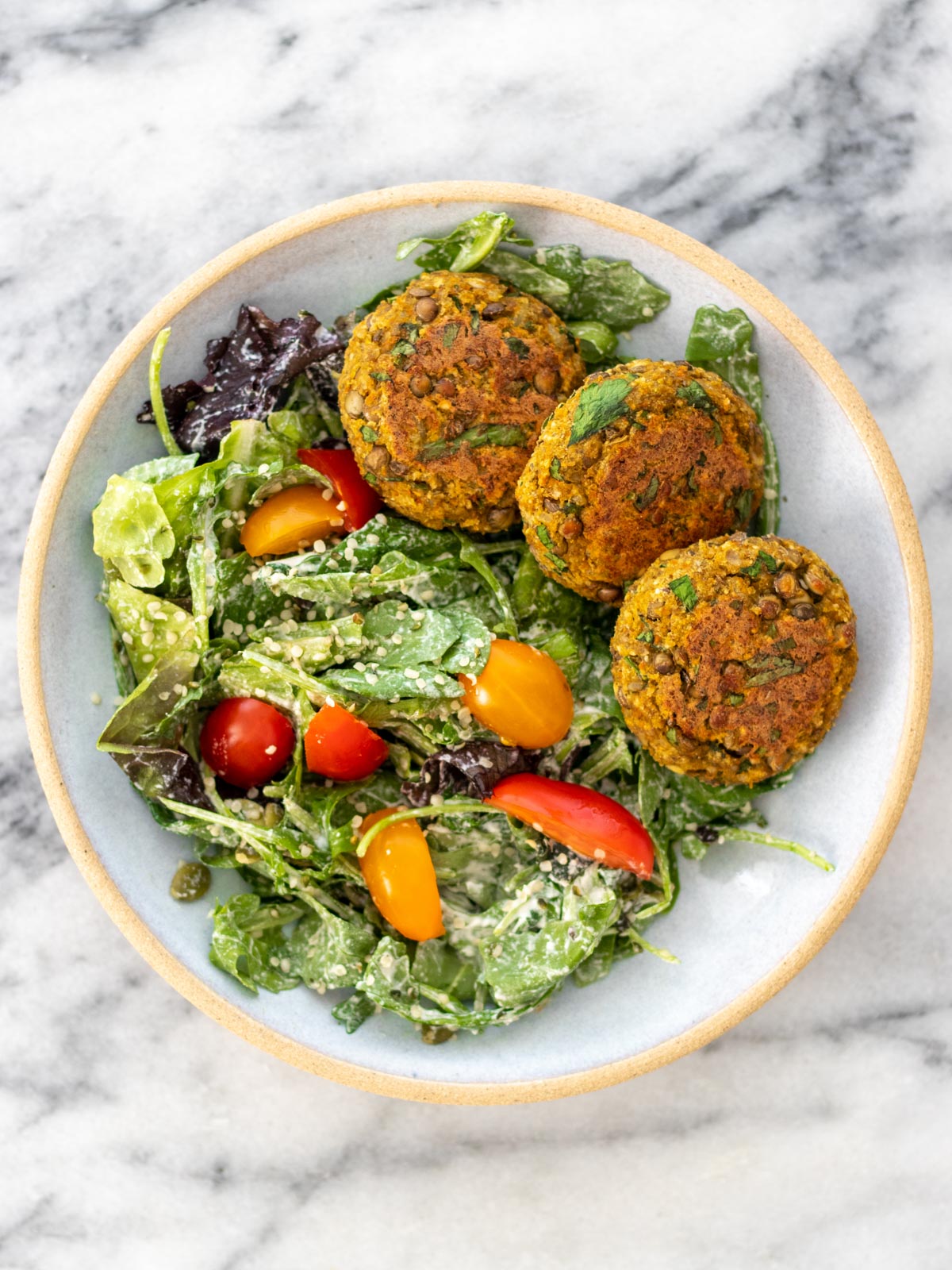 hambúrgueres de lentilha pequenos servidos com salada de folhas verdes e tomates-cereja