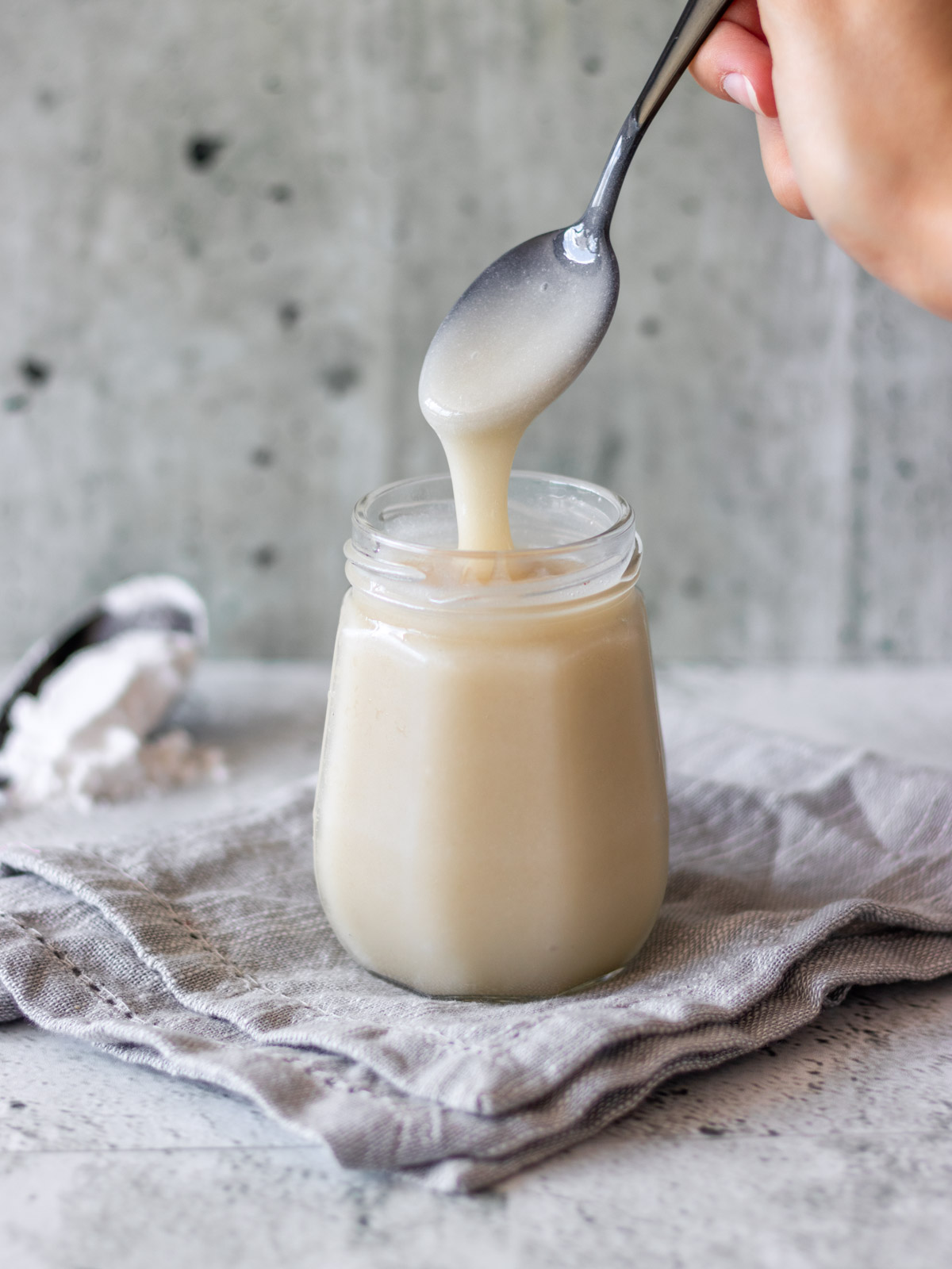 colher sendo retirado de pote de leite condensado vegano, mostrando sua textura cremosa
