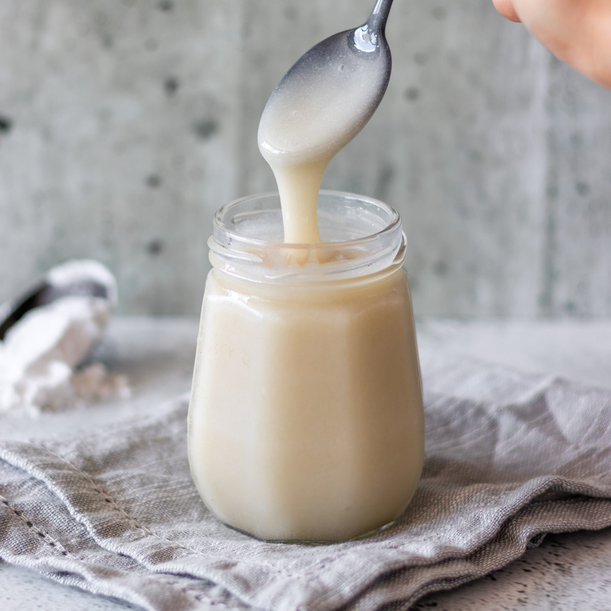 colher sendo retirado de pote de leite condensado vegano, mostrando sua textura cremosa