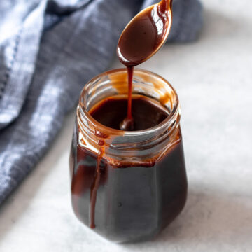 colher sendo retirada de pote de calda de chocolate sem leite, mostrando sua textura cremosa e cor brilhante