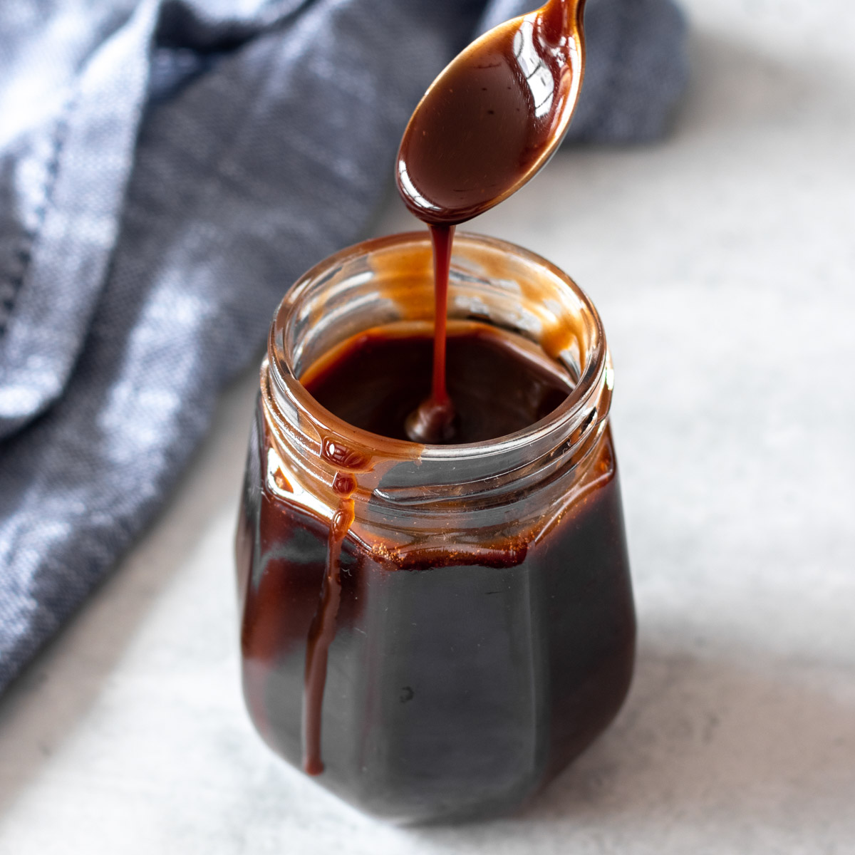 colher sendo retirada de pote de calda de chocolate sem leite, mostrando sua textura cremosa e cor brilhante